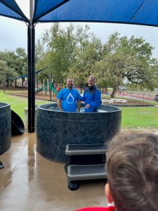 Erjon standing in an outdoor baptismal tank with a pastor on a rainy day, smiling.